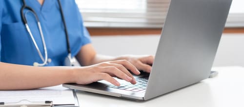 female-veterinarian-dressed-in-scrubs-wearing-stethoscope-typing-on-laptop