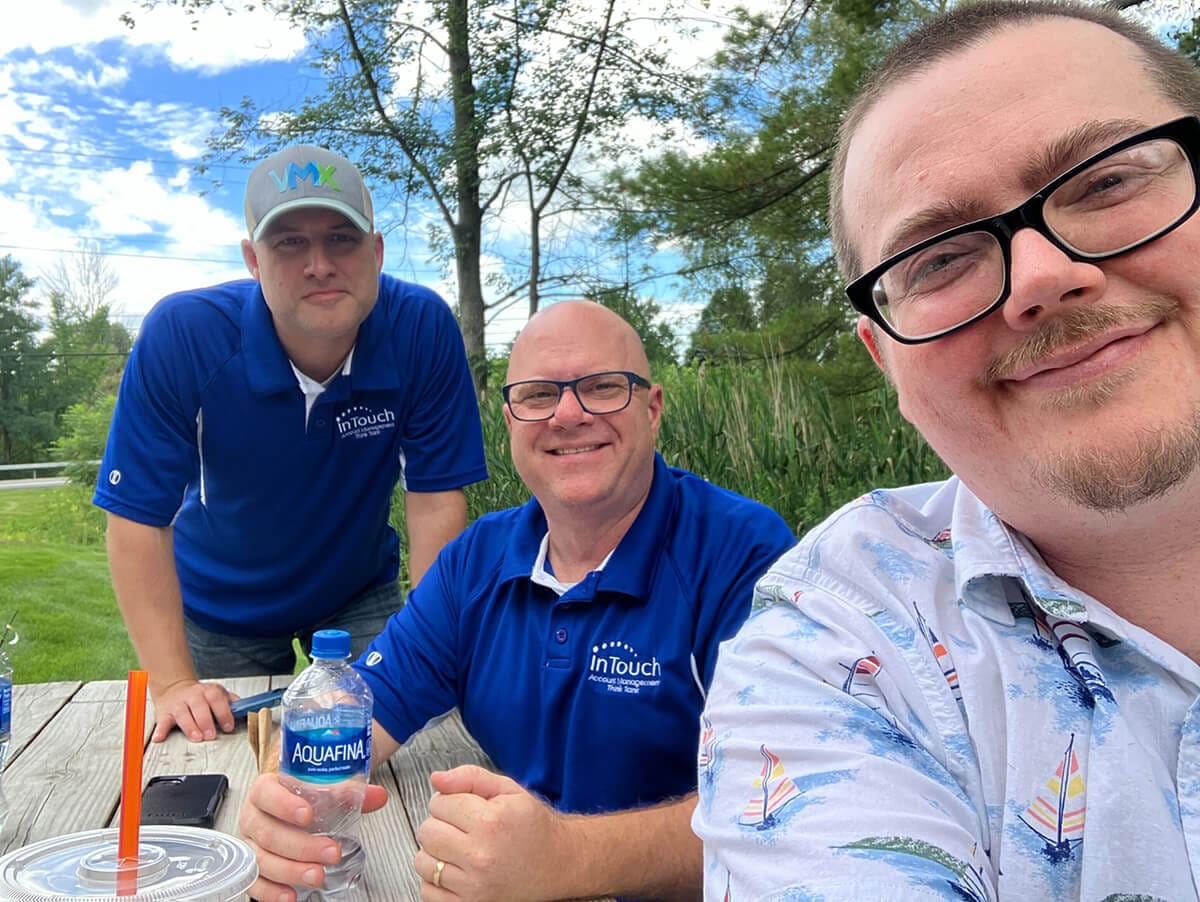 three men sitting at park bench outdoors smiling for camera