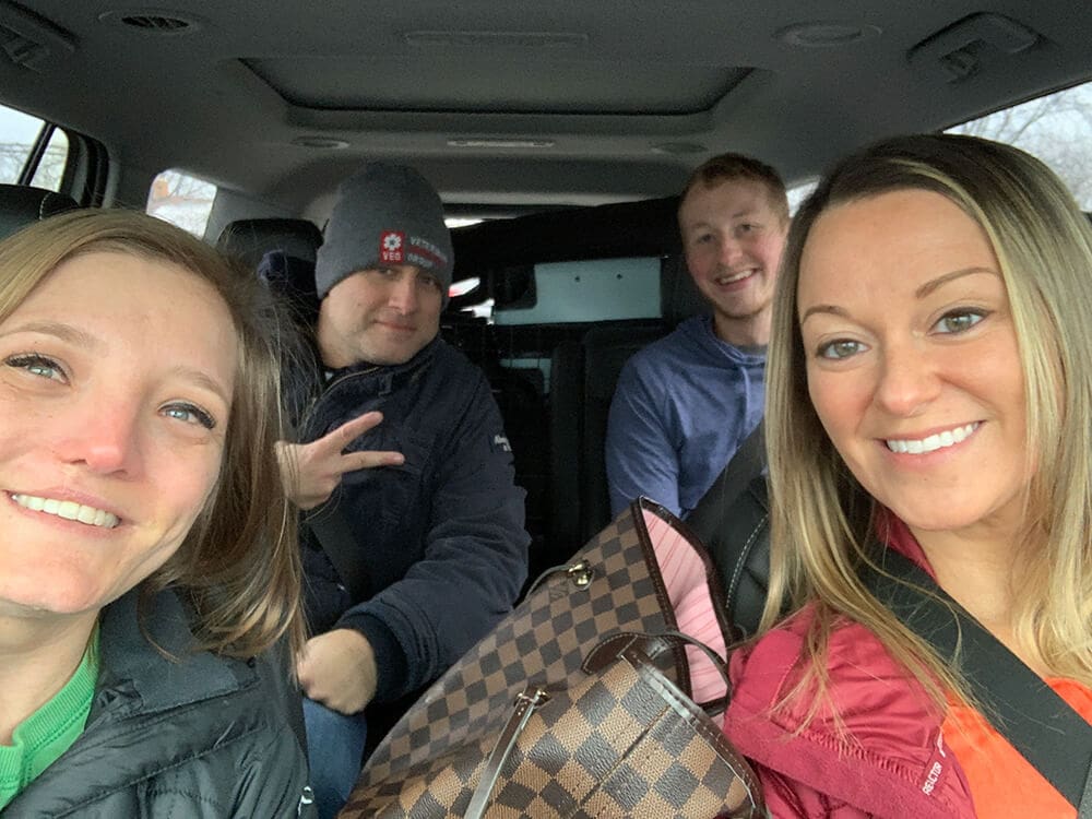 four people inside the back of a car smiling for camera
