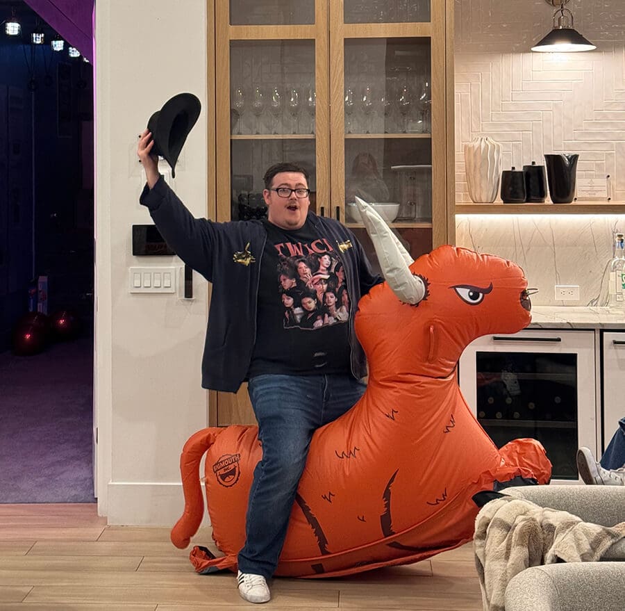 man riding orange inflatable bull in livingroom