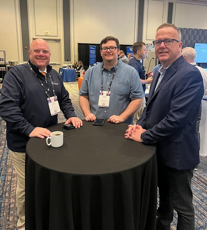 three men standing around a round table at a tradeshow
