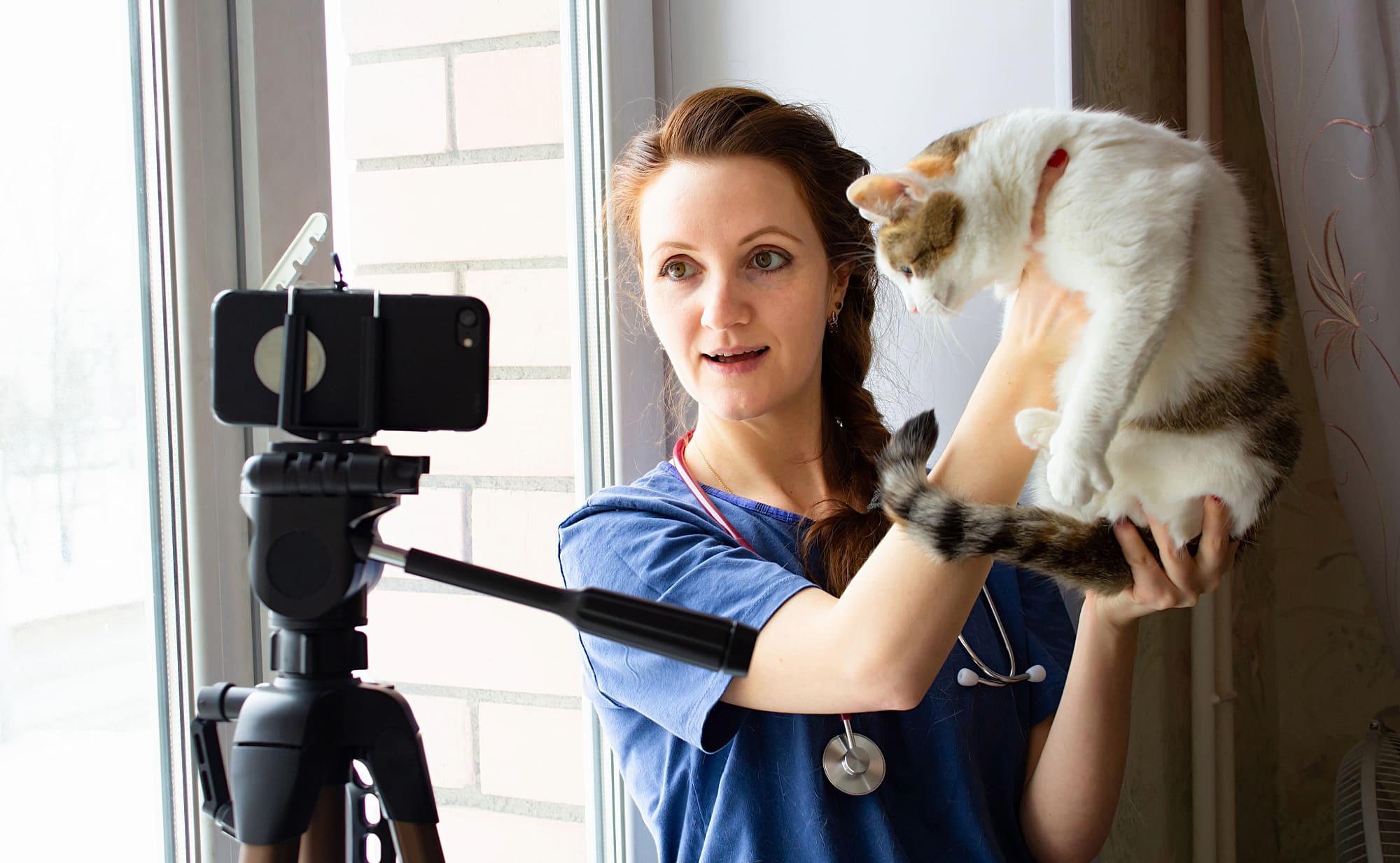 female veterinarian posing in front of a camera holding a cat
