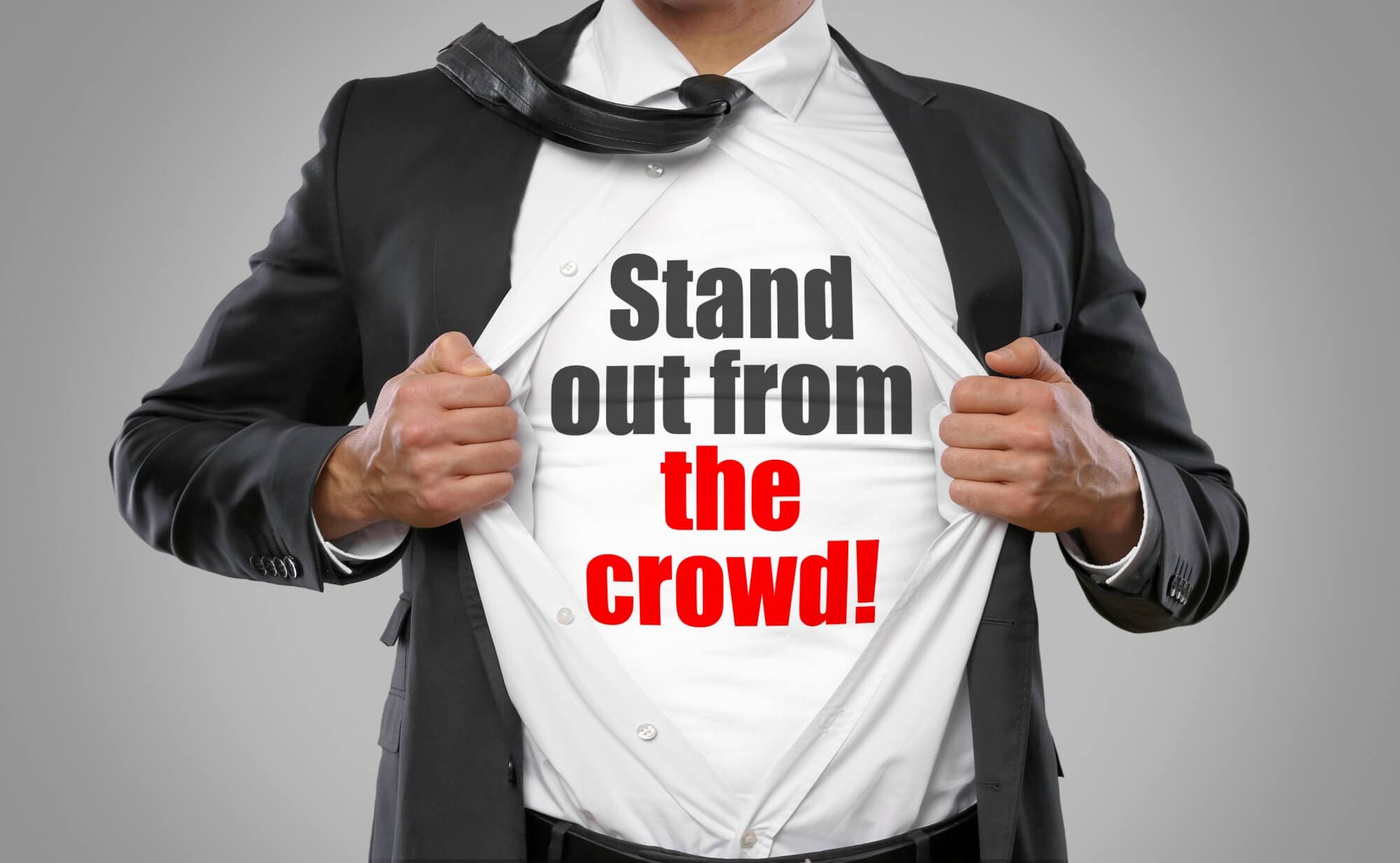 man wearing a suit, holding open button shirt to reveal tshirt that says "stand out from the crowed"